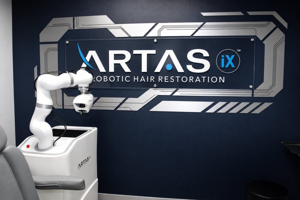 ARTAS iX robotic arm in front of the ARTAS Robotic Hair Restoration wall at Revive